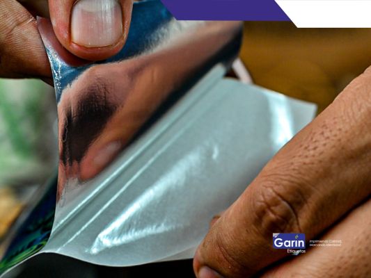 Es la fotografía de etiqueta metalizada siendo despegada por unas manos. Este es uno de los tipos de materiales más llamativos.